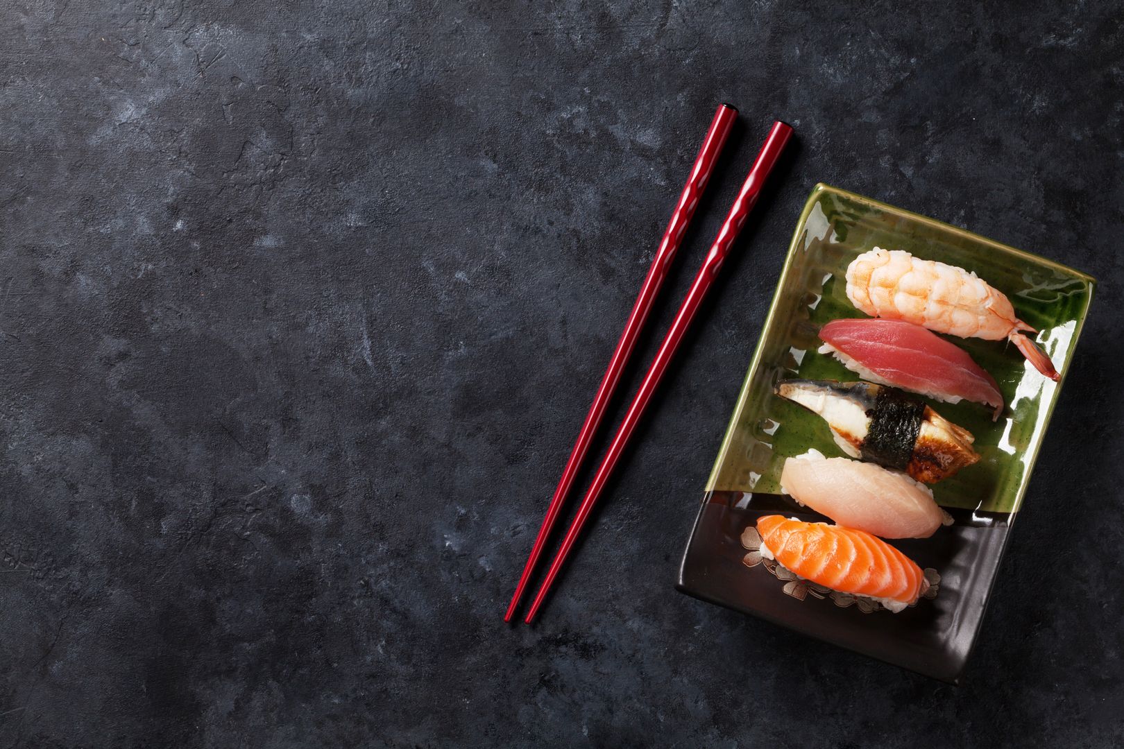 Sushi auf einem grünen Teller mit Stäbchen daneben